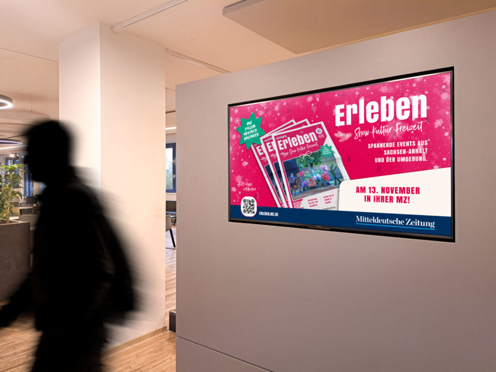 Digital‑Signage‑Motiv der Erleben Veranstaltungsbeilage 2025 auf Wandbildschirm in Innenraum
